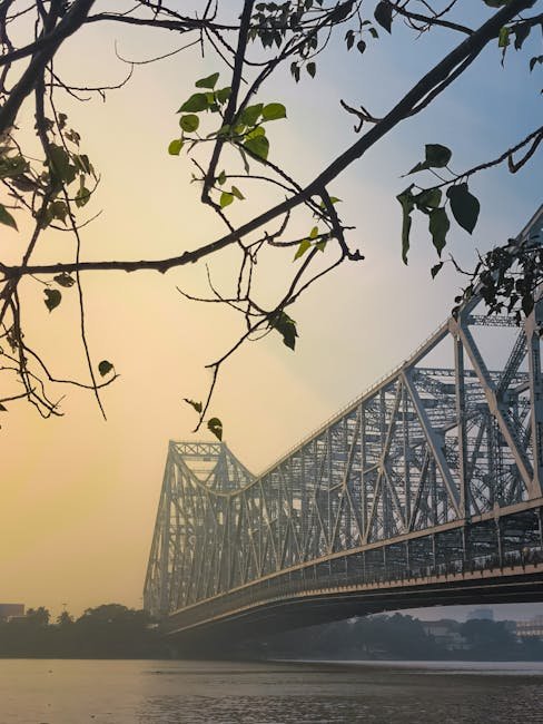 Beautiful dusk view of Howrah Bridge with silhouetted leaves and calm waters beneath.